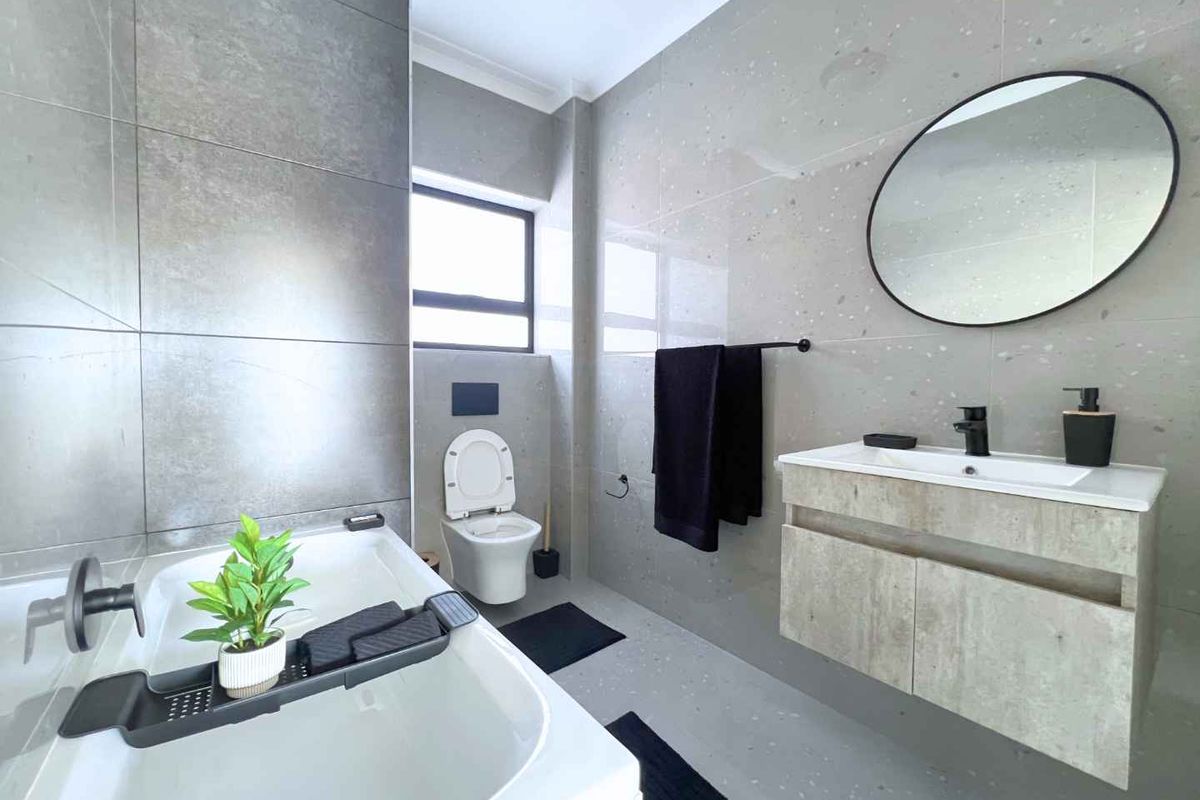 Modern bathroom featuring large-format grey tiling, a wall-mounted vanity with integrated basin, a wall-hung toilet, and a built-in bathtub.