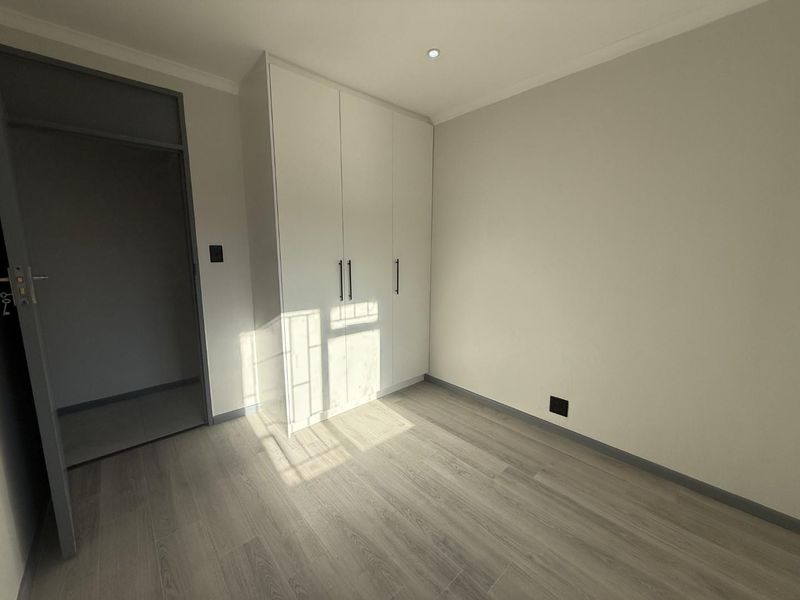 A bright, empty bedroom featuring modern laminate flooring, neutral walls, and clean white built-in cupboards.