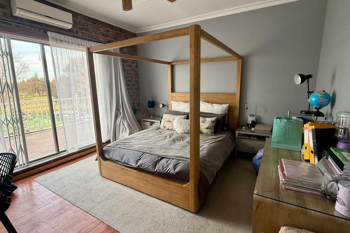 Spacious bedroom featuring an exposed brick accent wall, split-system air conditioning, ceiling fan, and large sliding glass doors leading to an outdoor balcony.