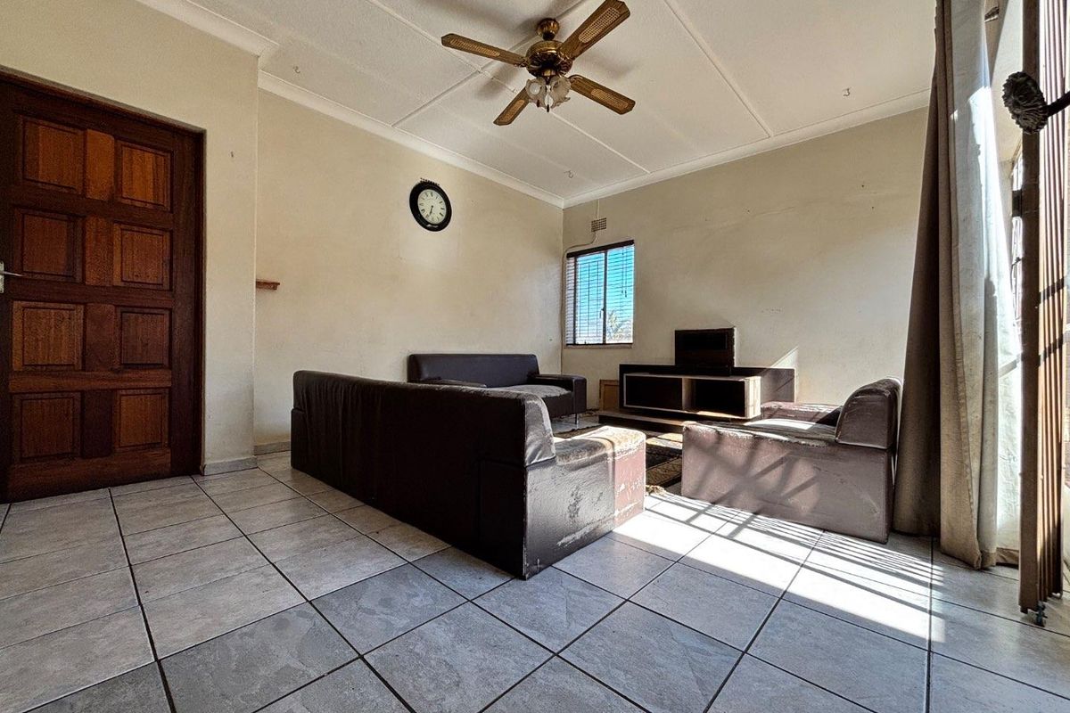 A living room featuring tiled flooring, a ceiling fan, and a wooden door, requiring cosmetic updates to improve its overall appeal.