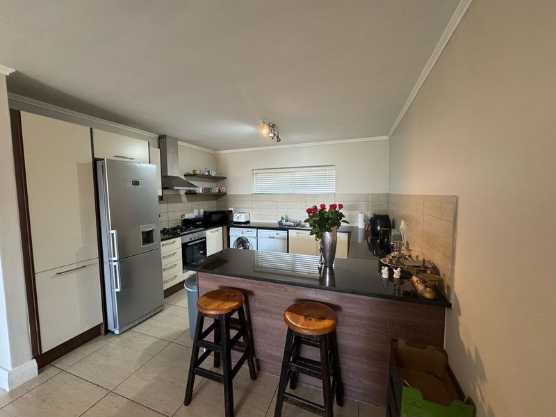 Modern kitchen featuring granite countertops, a breakfast bar, built-in oven, gas hob, extractor fan, and tiled flooring with ample storage cabinetry.