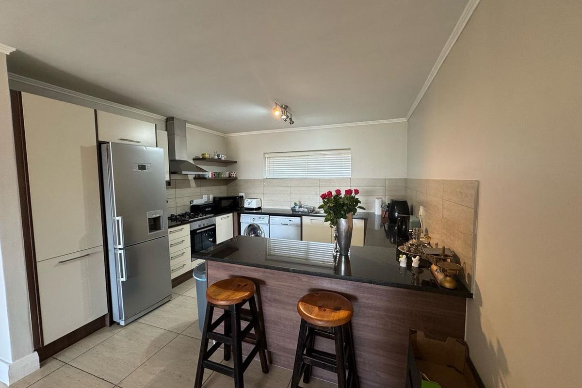 Modern kitchen featuring granite countertops, a breakfast bar, built-in oven, gas hob, extractor fan, and tiled flooring with ample storage cabinetry.