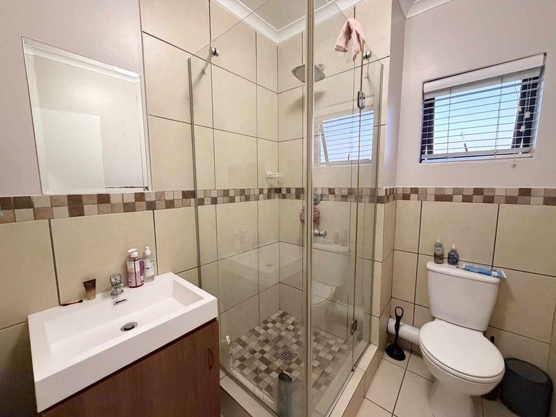 A functional bathroom featuring a glass-enclosed shower, wall-mounted vanity, toilet, and neutral tiled finishes throughout.