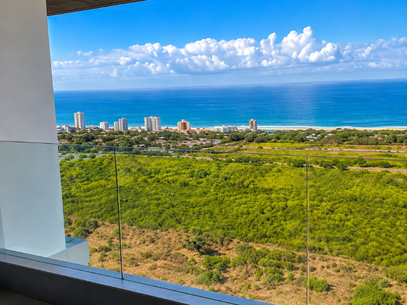 A modern balcony featuring a sleek glass balustrade and tiled flooring, offering expansive panoramic views of the coastline and surrounding landscape.