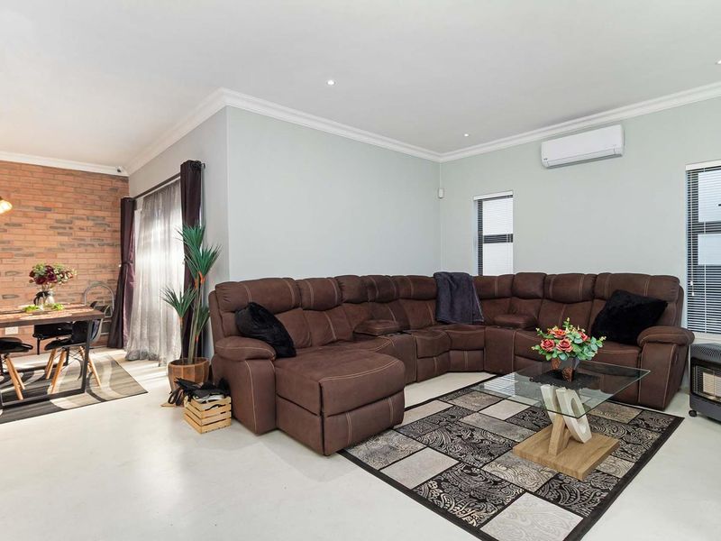 Spacious open-plan living and dining area featuring an exposed brick feature wall, recessed lighting, and a wall-mounted air conditioning unit.