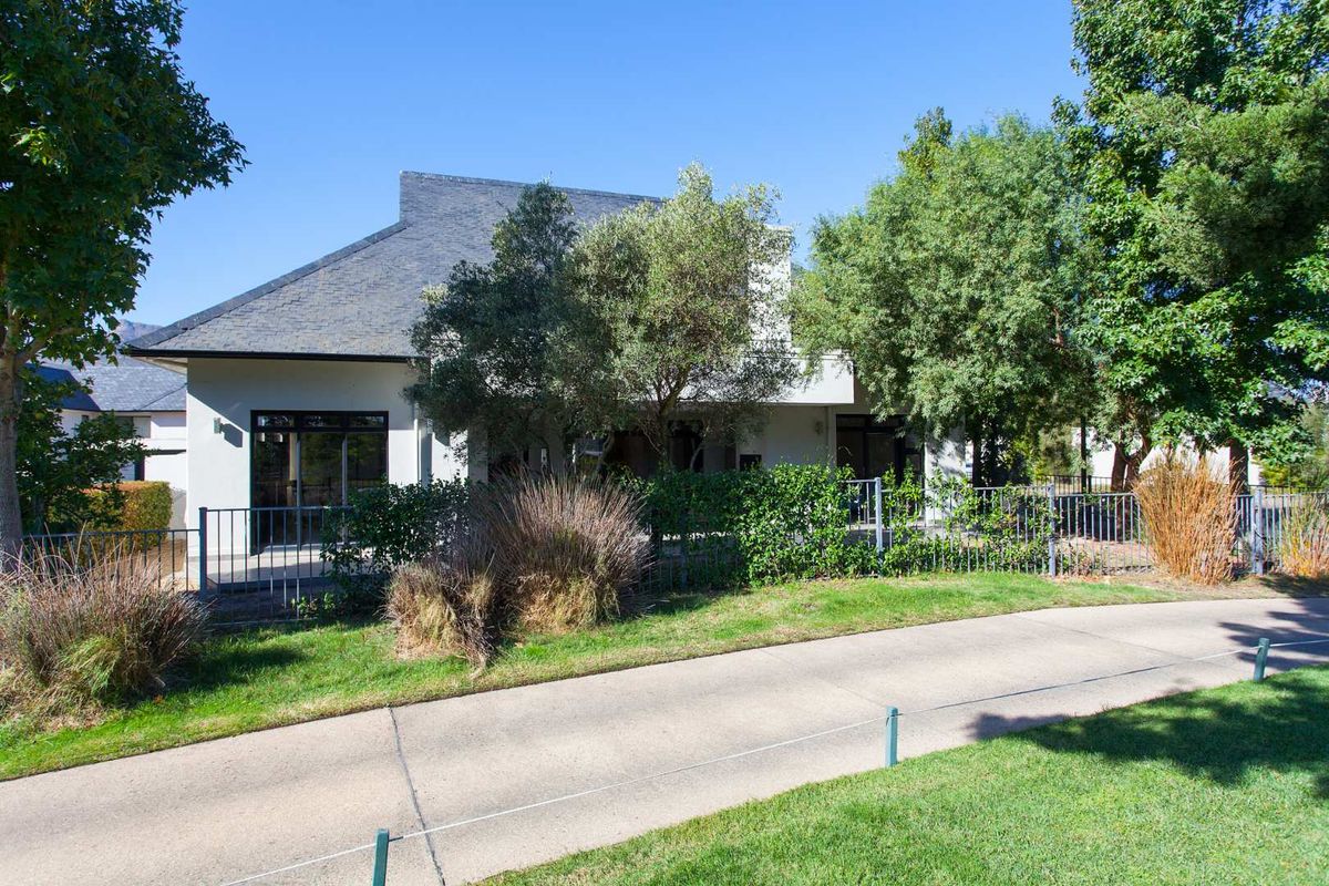 A view of the rear exterior of the house, featuring a paved patio area, established garden, and metal perimeter fencing.