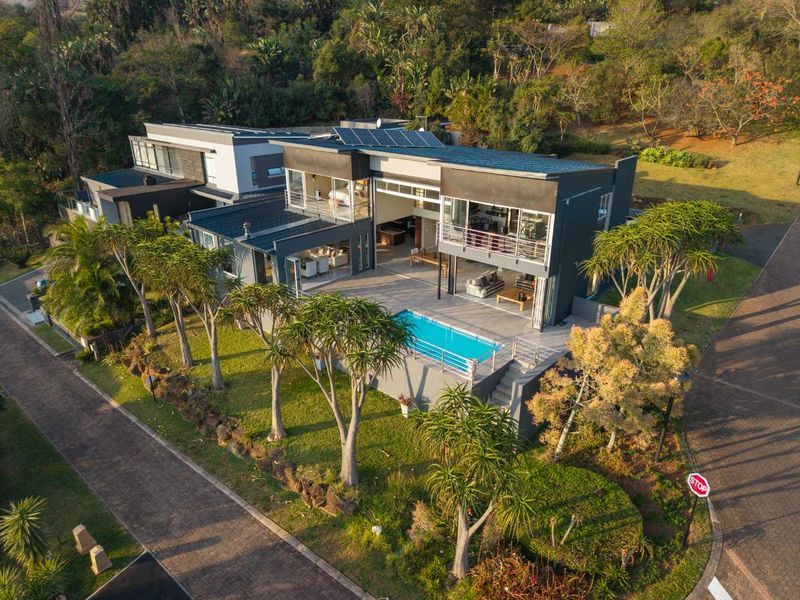 Aerial view of a modern multi-level residence featuring a swimming pool, expansive patio, balconies, and integrated solar panels set within a landscaped environment.