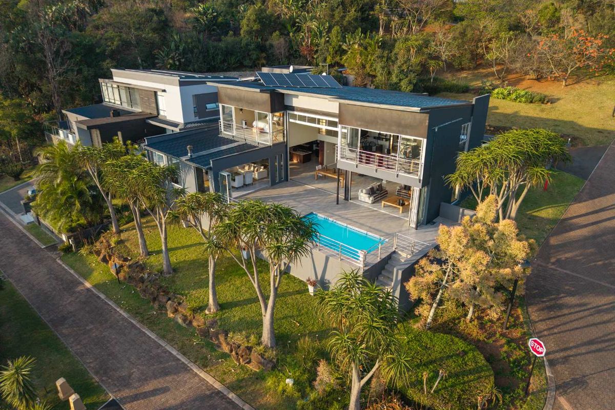 Aerial view of a modern multi-level residence featuring a swimming pool, expansive patio, balconies, and integrated solar panels set within a landscaped environment.
