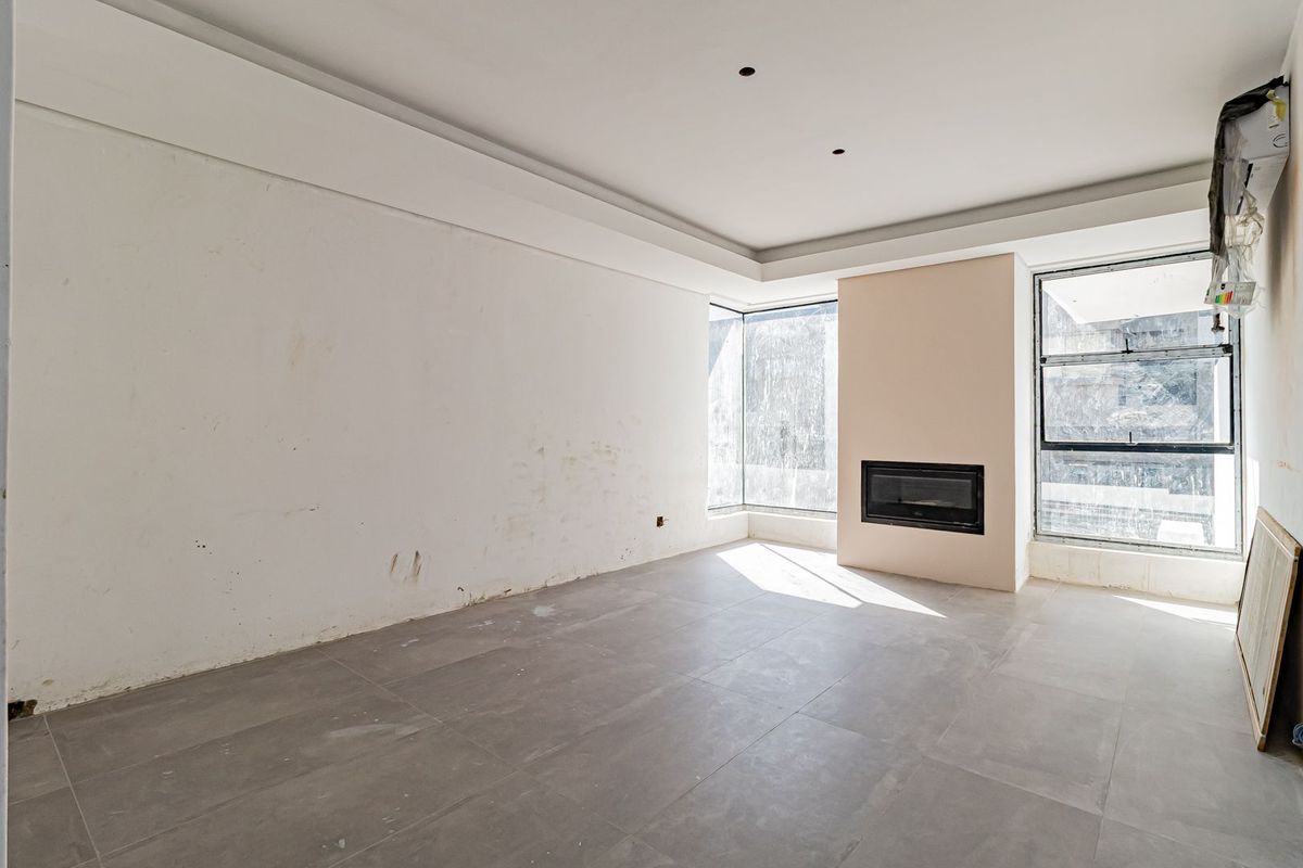 An empty living room featuring large format floor tiles, a built-in fireplace, and a corner window, currently requiring cosmetic wall finishing and cleaning.