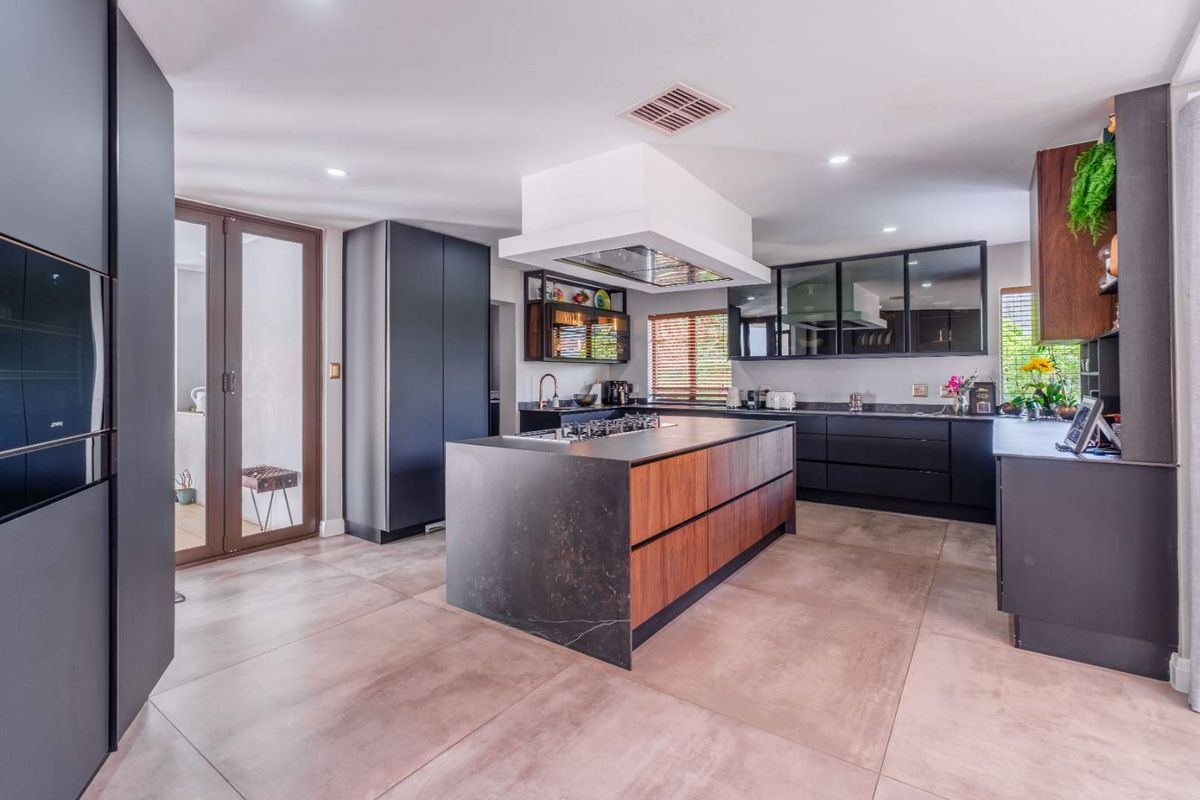 Modern kitchen featuring a large central island with a built-in gas hob, sleek dark cabinetry, stone countertops, and a contemporary overhead extractor fan.