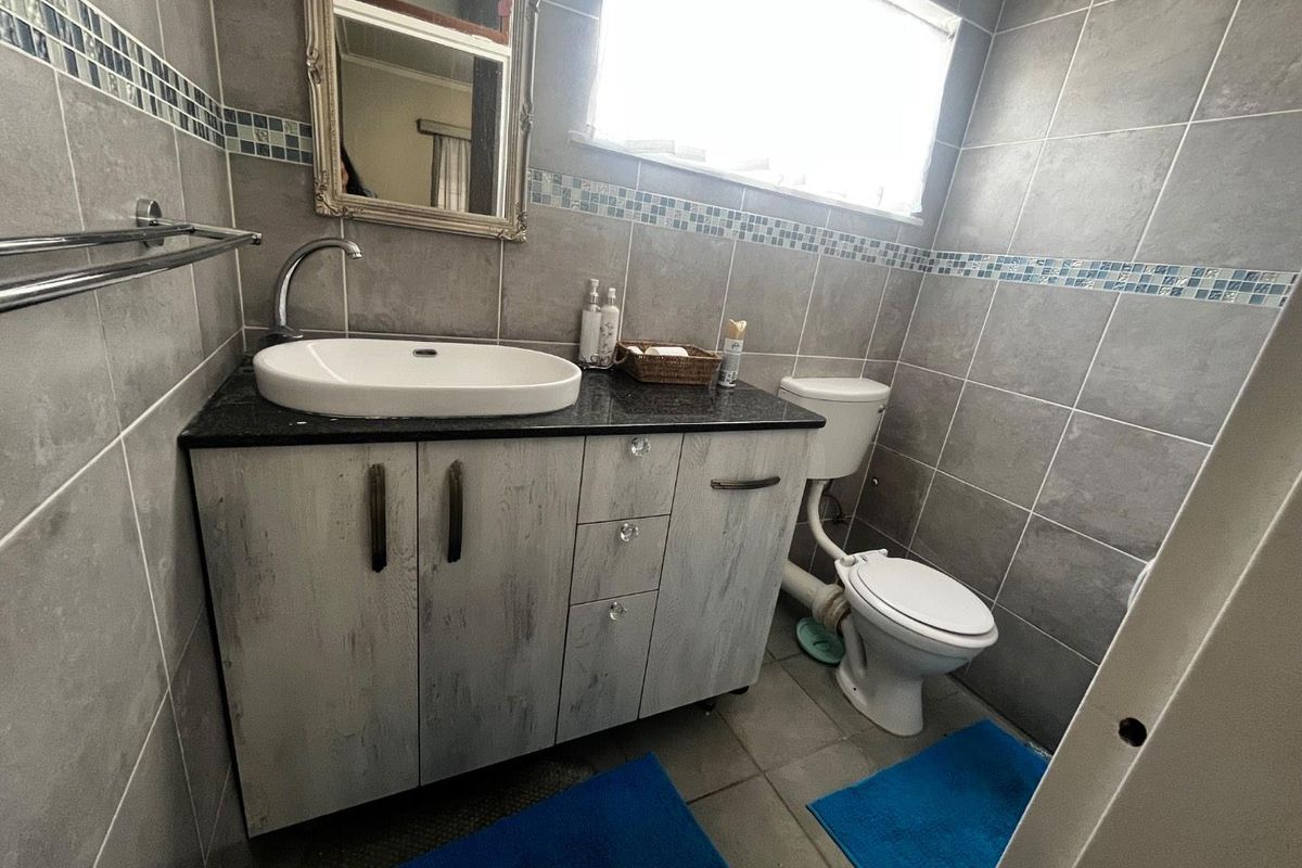 Compact bathroom featuring full-height grey wall tiling, a modern vessel sink on a vanity cabinet, and a standard toilet.