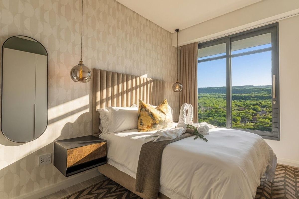 A well-appointed bedroom featuring patterned wallpaper, floating bedside tables, and a large sliding glass door offering expansive views of the surrounding landscape.