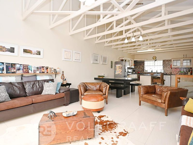 Spacious open-plan living and kitchen area featuring high vaulted ceilings with exposed white trusses and neutral tiled flooring throughout.