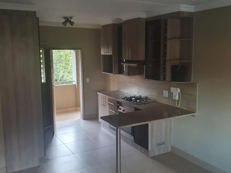 A functional kitchen featuring built-in cabinetry, a gas hob with extractor, and a breakfast bar, leading to an adjacent balcony area.