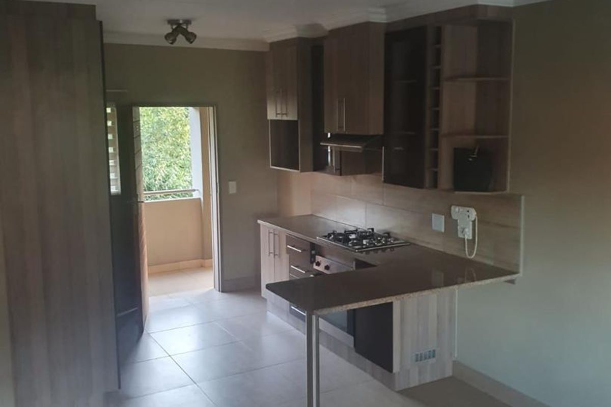 A functional kitchen featuring built-in cabinetry, a gas hob with extractor, and a breakfast bar, leading to an adjacent balcony area.