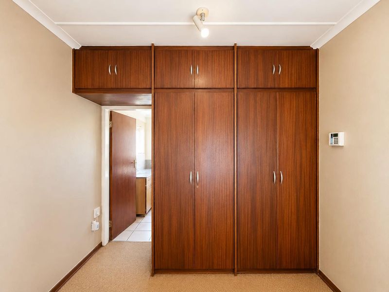 A bedroom featuring extensive built-in wooden cupboards with overhead storage, neutral carpeting, and a security alarm keypad.
