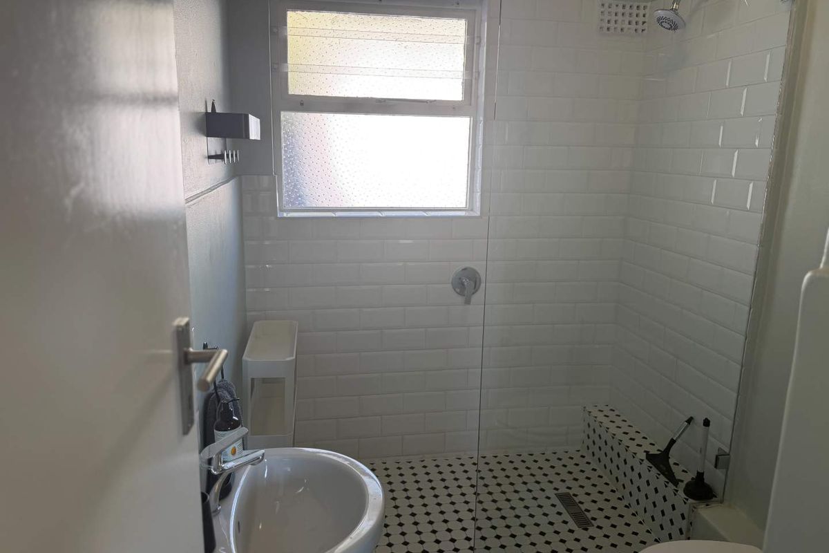 A modern bathroom featuring a walk-in shower with white subway tiles, a glass partition, and classic black and white mosaic floor tiling.