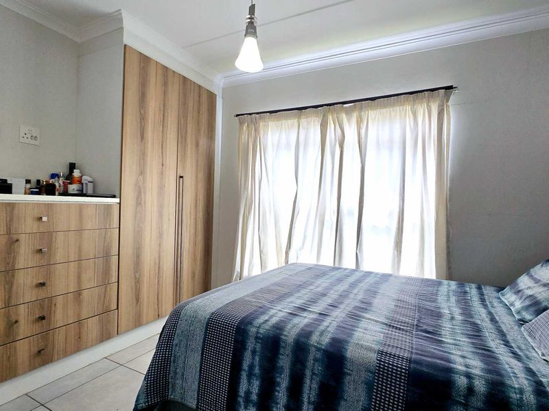 A well-maintained bedroom featuring modern built-in cupboards, tiled flooring, and crown molding, providing a clean and functional living space.