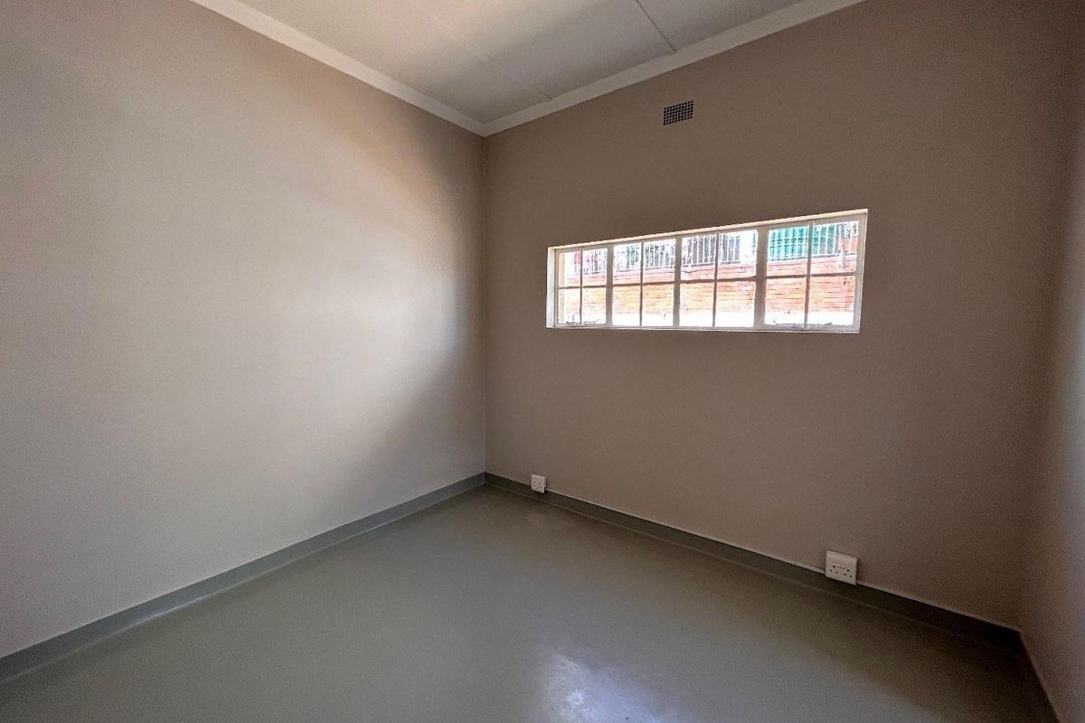 A clean, empty room featuring neutral painted walls, vinyl flooring, and a high-set window with security bars.