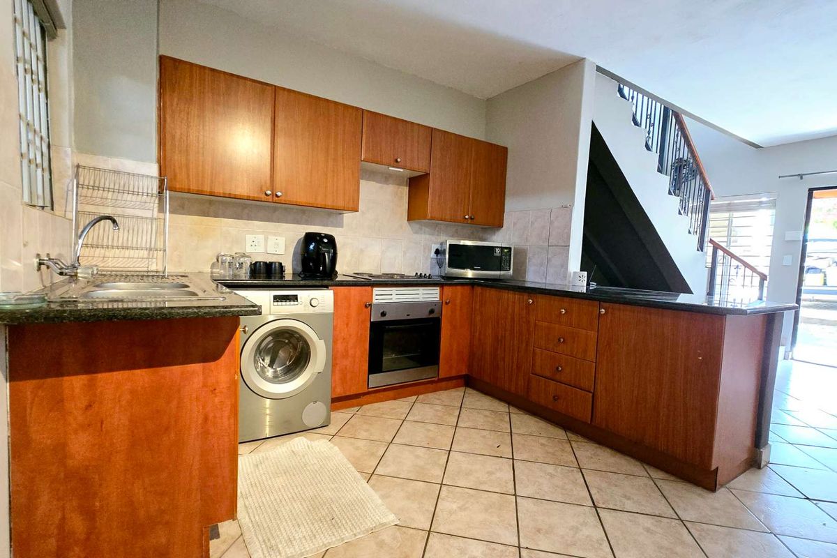 Functional kitchen featuring wood-veneer cabinetry, granite countertops, built-in oven, hob, and extractor fan, with an integrated laundry space under the counter.