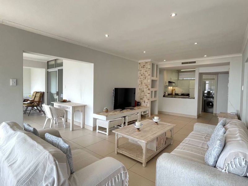 Spacious open-plan living area featuring tiled floors, recessed lighting, and a stone-accented built-in shelving unit, seamlessly connecting to the kitchen and dining space.