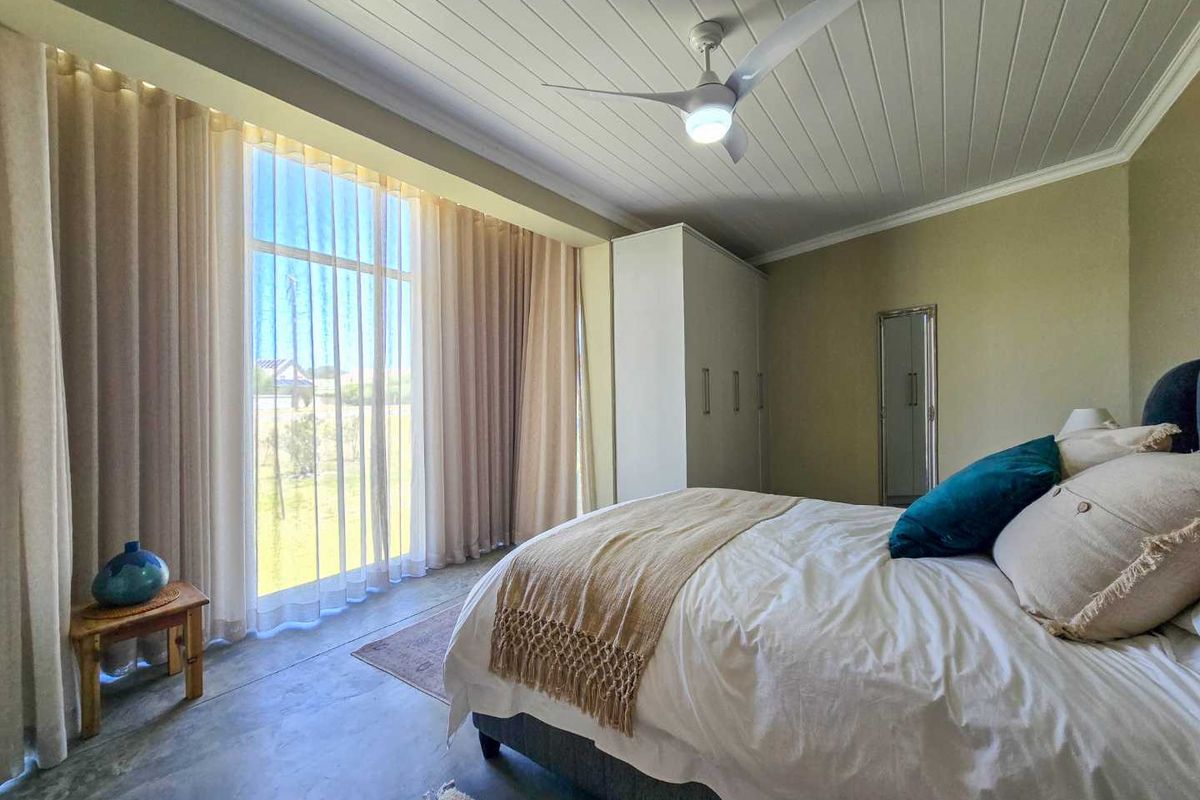 Spacious bedroom featuring polished concrete floors, a tongue and groove ceiling with a fan, and large windows providing ample natural light.