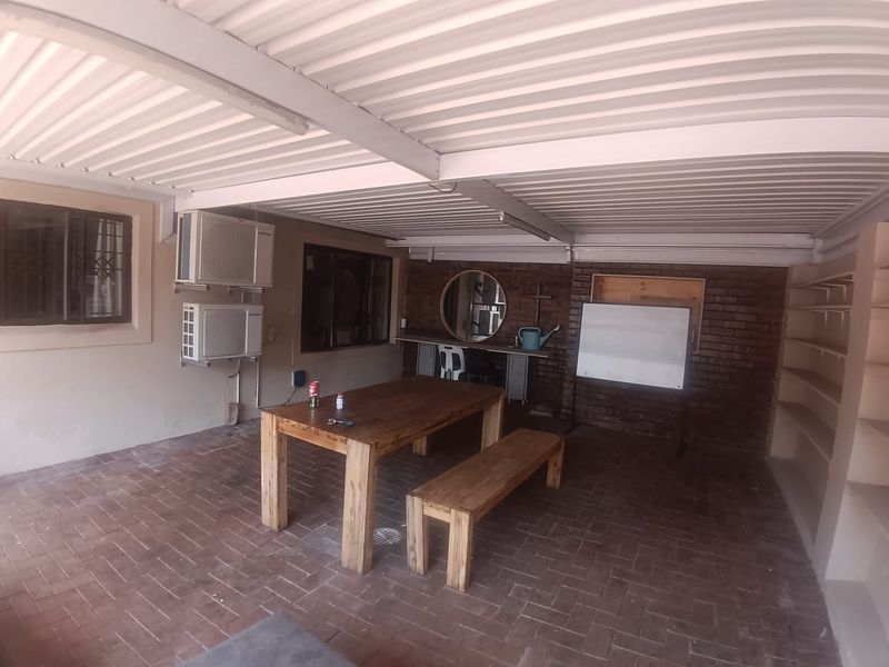 A covered outdoor patio area featuring brick flooring, exposed brick walls, built-in shelving, and wall-mounted air conditioning units.