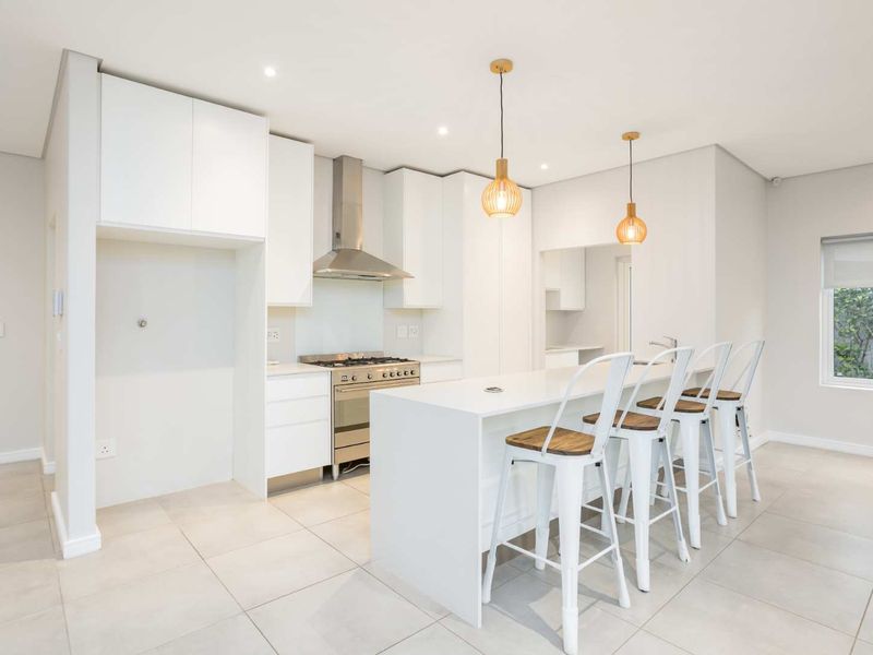 Modern, bright kitchen featuring white cabinetry, a central island, stainless steel gas stove, extractor fan, and neutral tiled flooring.