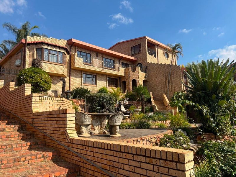A multi-level face brick residence featuring extensive terraced landscaping, brick retaining walls, and multiple balconies overlooking the rear garden area.