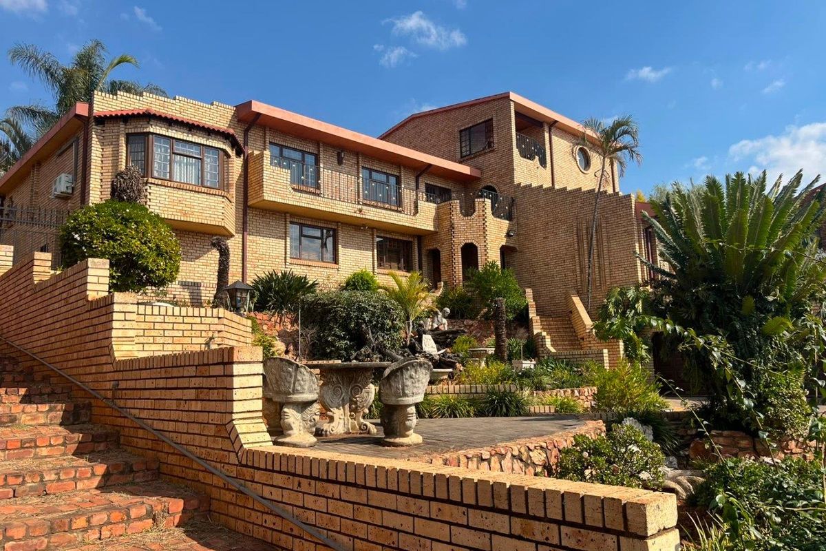 A multi-level face brick residence featuring extensive terraced landscaping, brick retaining walls, and multiple balconies overlooking the rear garden area.
