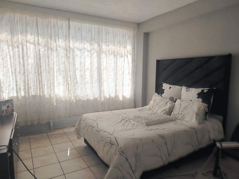 A bedroom featuring tiled flooring and a large window with sheer curtains, providing natural light to the space.