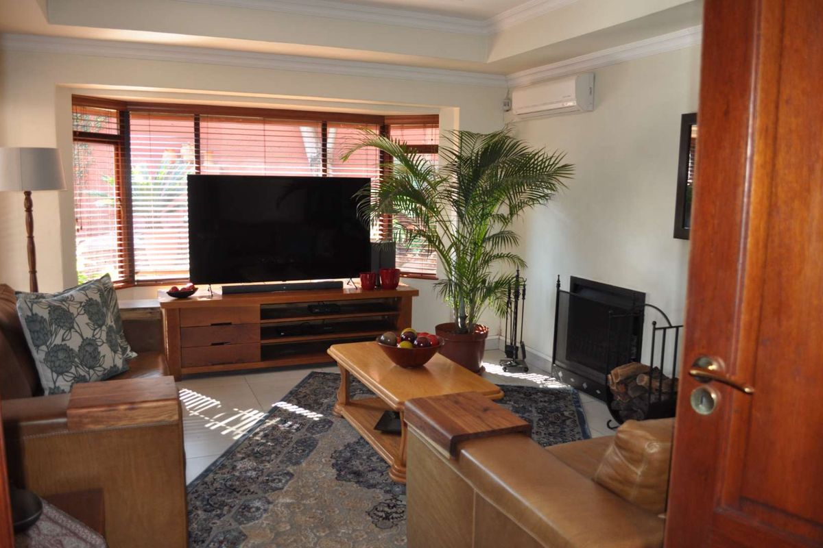 A comfortable living room featuring a bay window, a fireplace, and a split-system air conditioner, finished with tiled flooring and cove ceiling detailing.