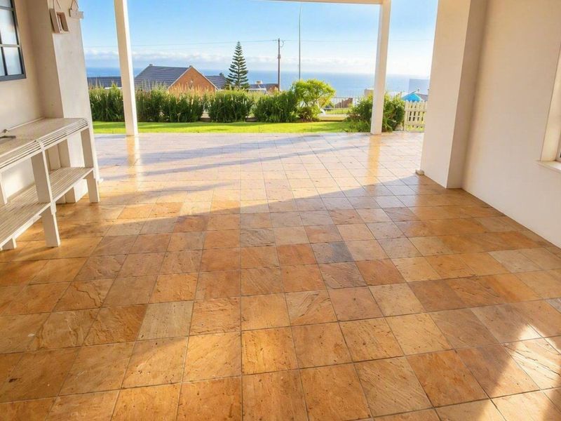 A spacious covered patio featuring natural stone-look tiles, offering an open-air transition to the garden with scenic coastal views.