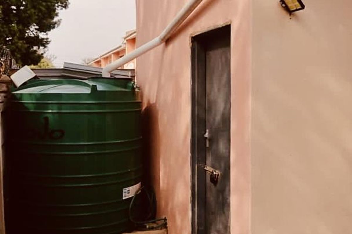Exterior view of a utility area featuring a large green water storage tank, brick paving, and a secure access door.