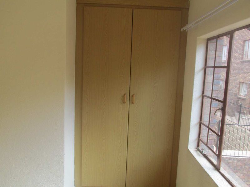 A bedroom featuring a built-in wooden wardrobe and a window with security bars overlooking the exterior.
