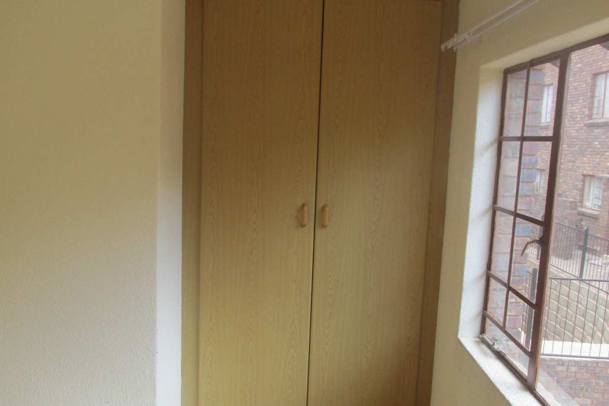 A bedroom featuring a built-in wooden wardrobe and a window with security bars overlooking the exterior.
