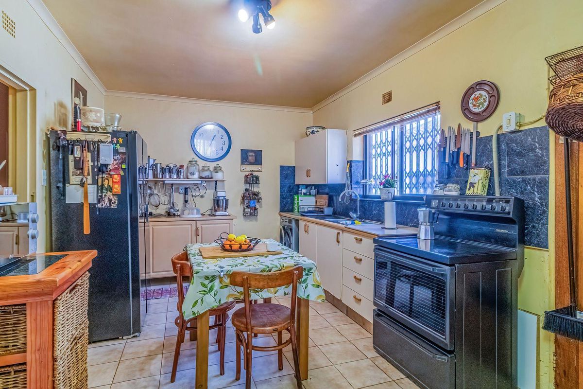 A functional kitchen featuring tiled flooring, built-in cabinetry, a tiled backsplash, and a window fitted with a security gate.