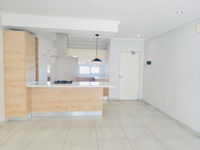 Modern open-plan kitchen and living area featuring light wood cabinetry, stone countertops, integrated gas hob, extractor fan, and neutral tiled flooring throughout.