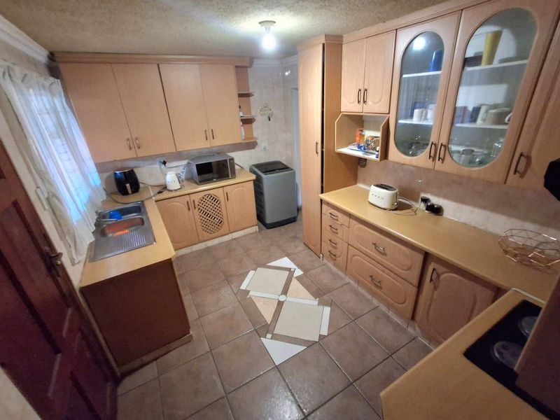A functional kitchen featuring extensive laminate cabinetry, double bowl sink, and tiled flooring, offering a dated aesthetic ready for modernization.
