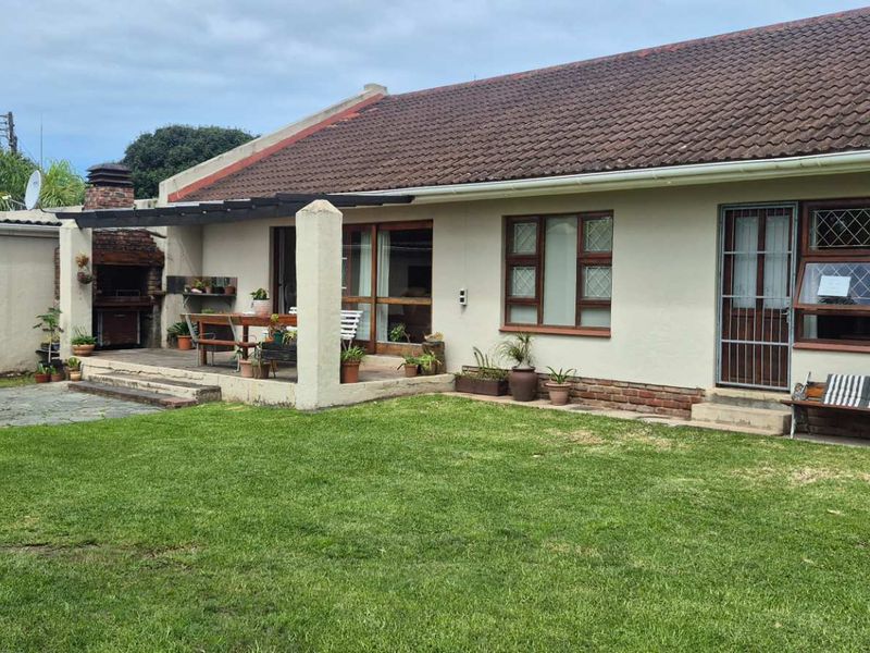 Rear view of the house featuring a lawn, a covered patio area with a built-in braai, and access to the interior via sliding doors.