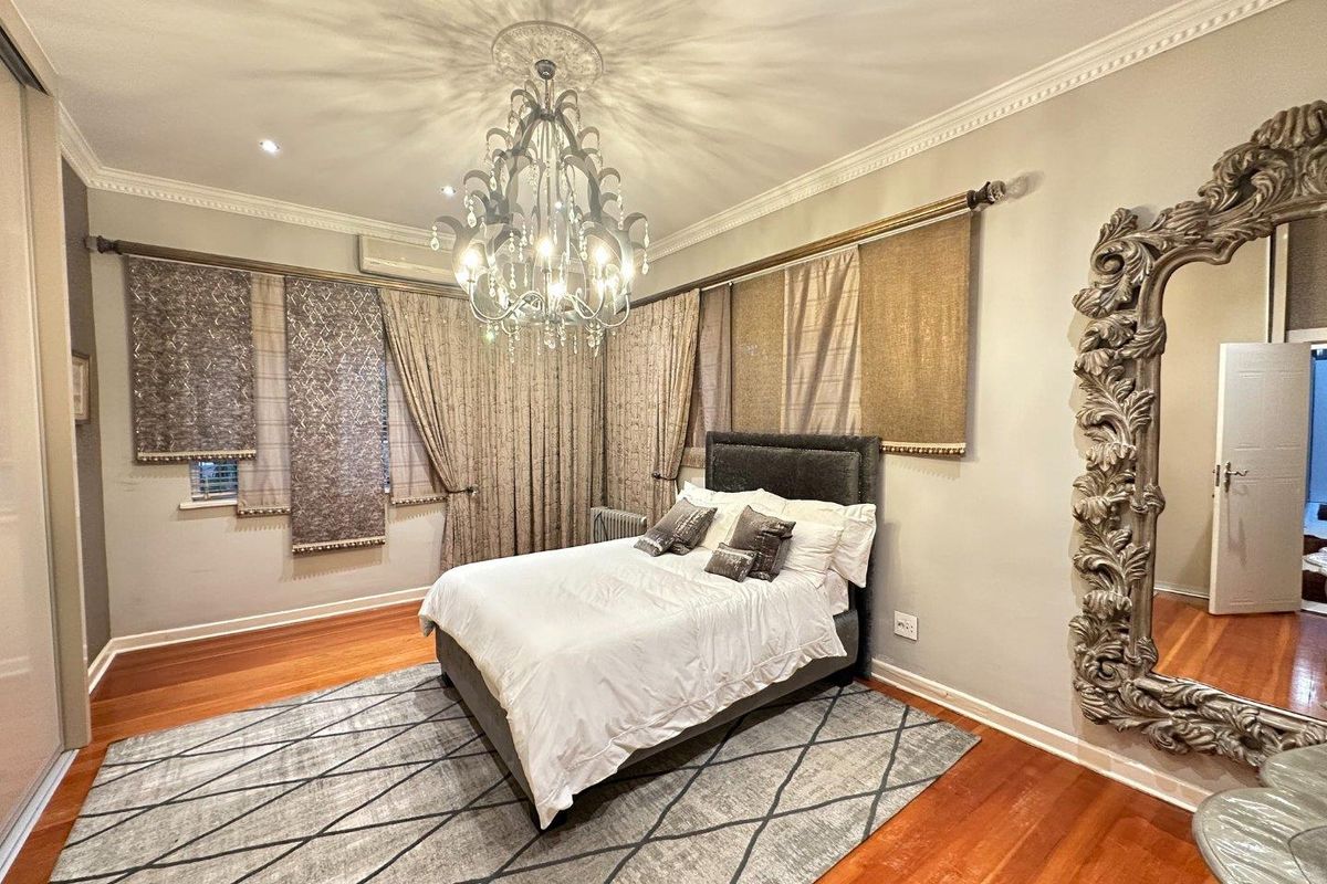 Spacious bedroom featuring polished timber flooring, decorative ceiling rose with chandelier, and built-in sliding door wardrobe.