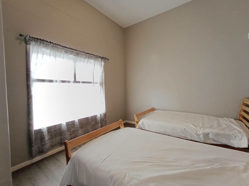 A simple bedroom featuring neutral wall tones, laminate flooring, and a window with a curtain rod.