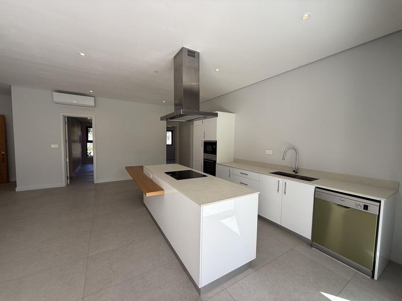 Modern, minimalist kitchen featuring a central island with an induction hob, integrated appliances, stone countertops, and sleek white cabinetry in an open-plan layout.