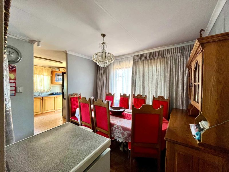 A traditional dining room featuring a decorative crystal chandelier and coving, with an open-plan flow leading into the adjacent kitchen area.
