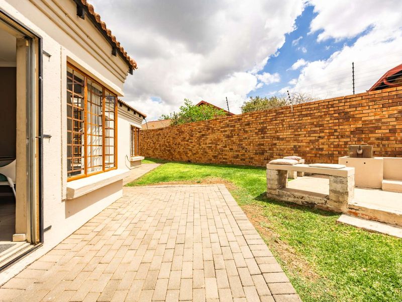 Rear garden area featuring a paved patio, built-in braai, and high brick boundary walls with electric fencing.