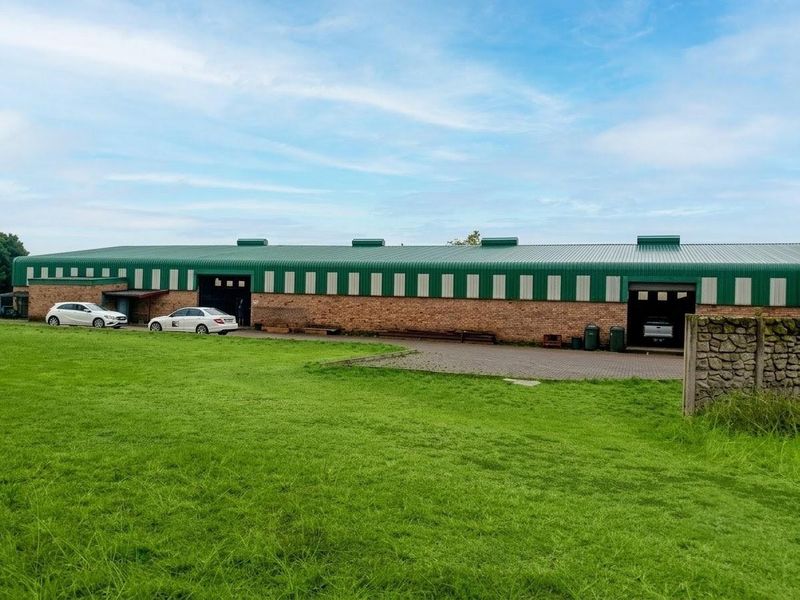 Rear view of a large commercial warehouse building featuring a brick exterior, corrugated metal roof, and an adjacent paved driveway area.