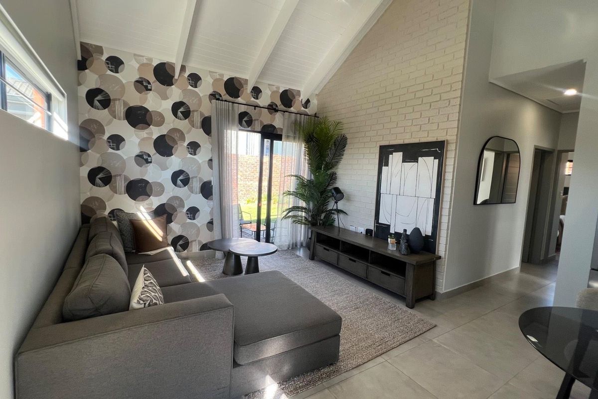 Spacious living room featuring a vaulted ceiling with exposed beams, a textured brick feature wall, and large sliding doors leading to the garden.
