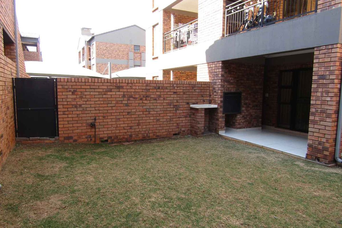 A private rear garden featuring a brick boundary wall, a small lawn area, and a covered patio with a built-in braai.