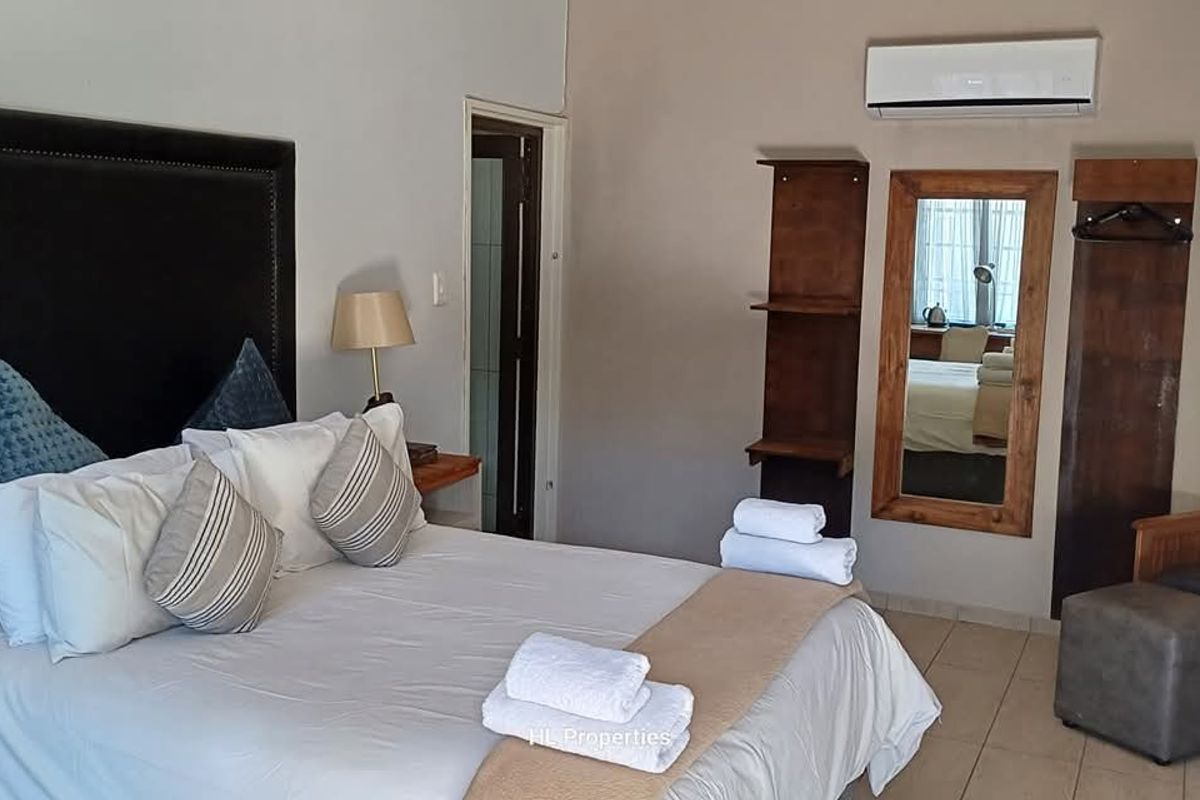 A guest bedroom featuring tiled flooring, a wall-mounted air conditioning unit, and built-in wooden shelving with an integrated mirror.