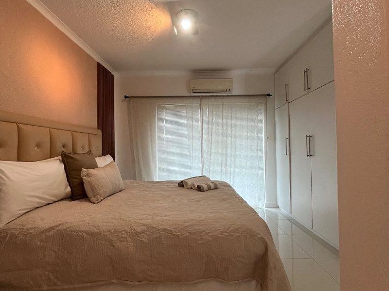 A well-maintained bedroom featuring built-in cupboards, tiled flooring, and an integrated air conditioning unit, with access to a balcony through sliding doors.